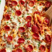 Pizza Pasta topped with Pepperoni in a casserole dish with a wooden spoon in it.