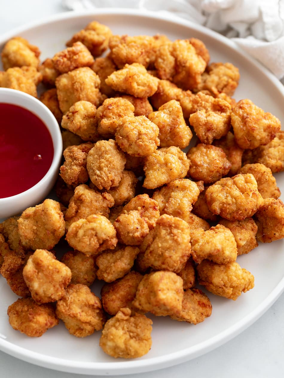 Popcorn Chicken on a white plate with a ramekin of sweet and sour sauce on the side.