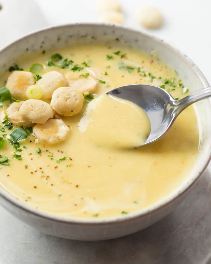 A bowl of Potato Leek Soup with a spoon and oyster crackers and parsley on the side.