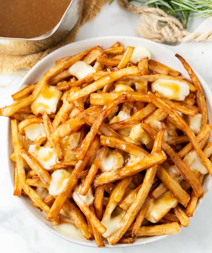 A white plate full of homemade poutine with french fries, gravy, and melted cheese curds.