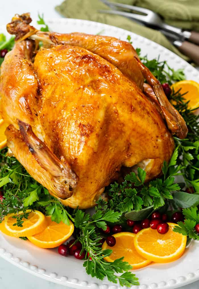 A roast turkey on a white platter with green parsley, sliced oranges, and fresh cranberries.