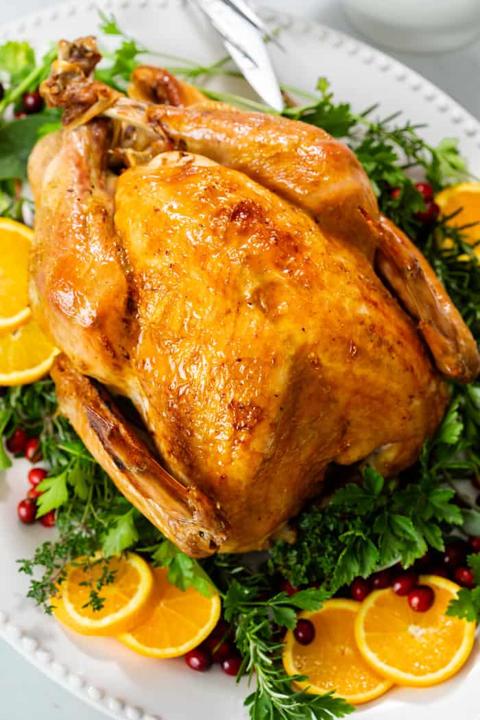 A golden roast turkey on a large serving platter with fresh herbs.