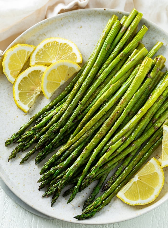 A white plate with roasted asparagus on top with sliced lemons.