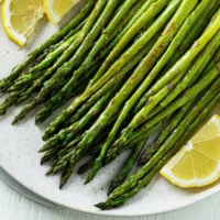 A plate topped with roasted asparagus and lemon wedges.