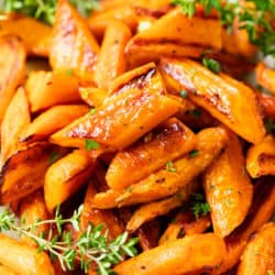 Sliced up roasted carrots piled on top of each other with fresh thyme on the side and in the back.
