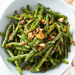 A white bowl filled with roasted green beans with thinly sliced almonds on top.