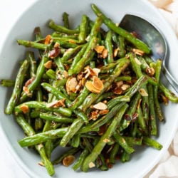 A white bowl of roasted green beans topped with sliced almonds.
