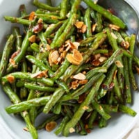 A bowl of roasted green beans topped with crispy sliced almonds.