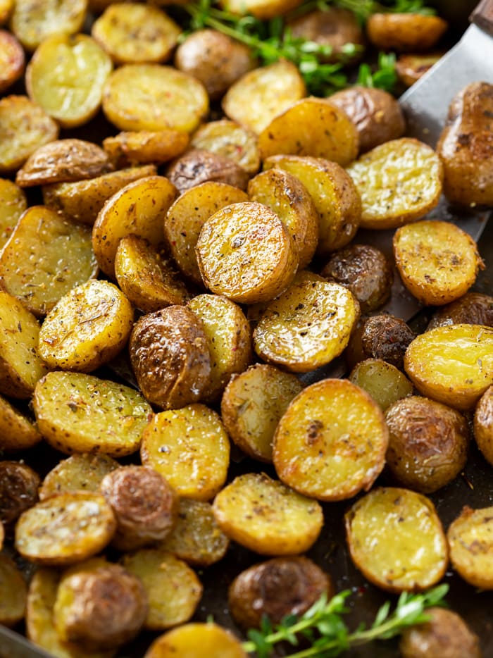Roasted potatoes with seasoning on top on a baking sheet with fresh thyme.