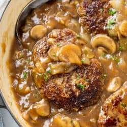 A skillet with Salisbury Steak in a thick mushroom gravy topped with fresh parsley.