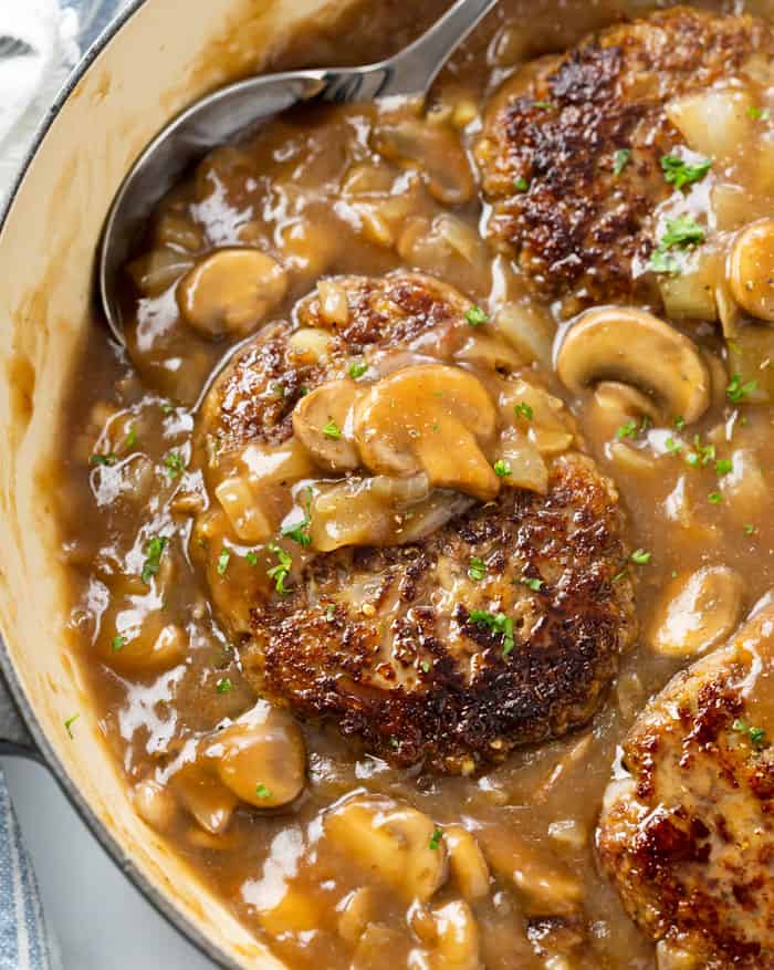 A skillet with Salisbury Steak in a thick mushroom gravy topped with fresh parsley.