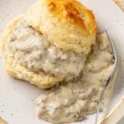 A buttermilk biscuit slice in half and topped with Sausage Gravy with a fork on the side.