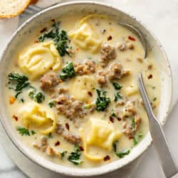 A bowl of creamy sausage tortellini soup with kale and a spoon.
