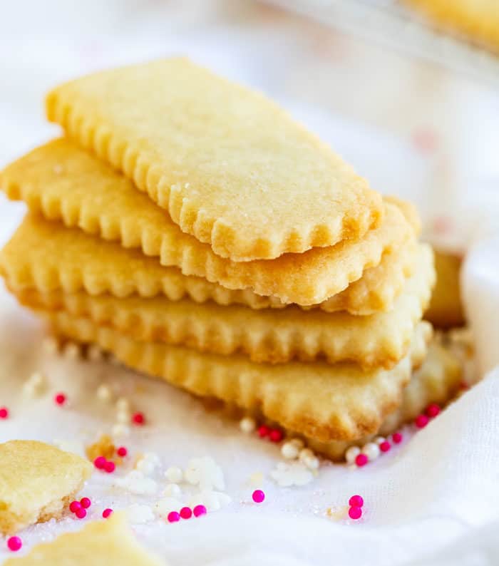 A stack of shortbread cookies on a white surface with sprinkles around it.