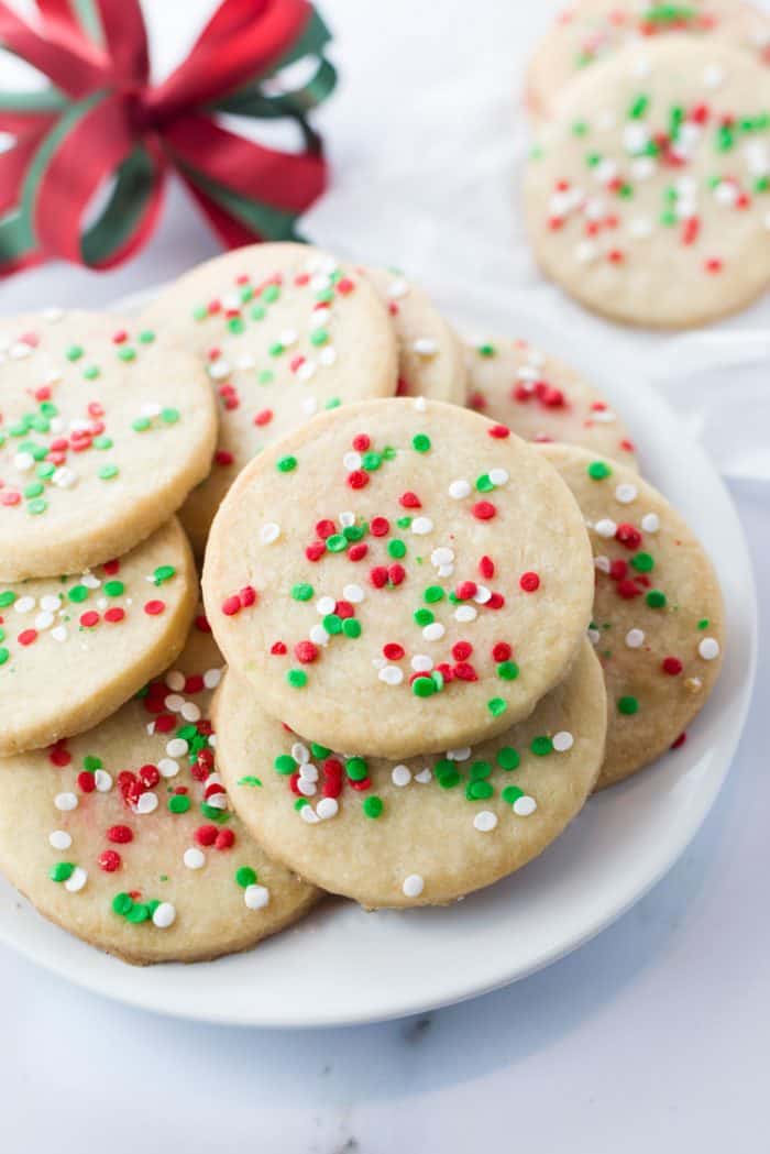 Shortbread cookies on a white plate with a red holiday bow in background