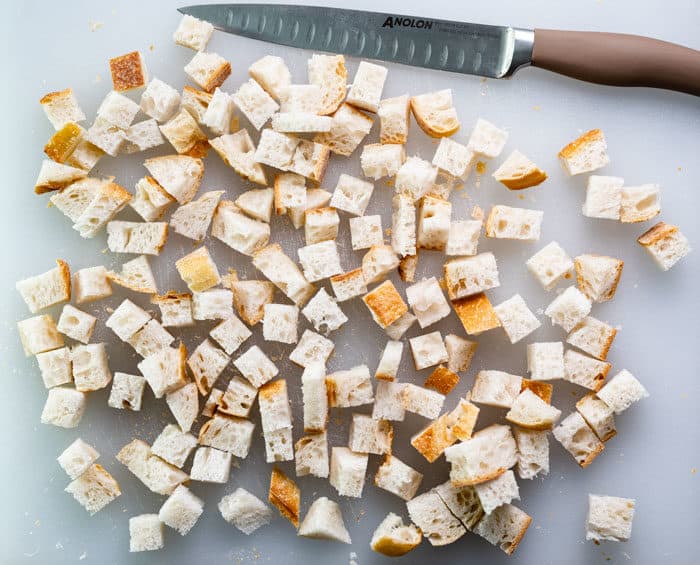 bread on a cutting board cut into cubes for homemade croutons. 