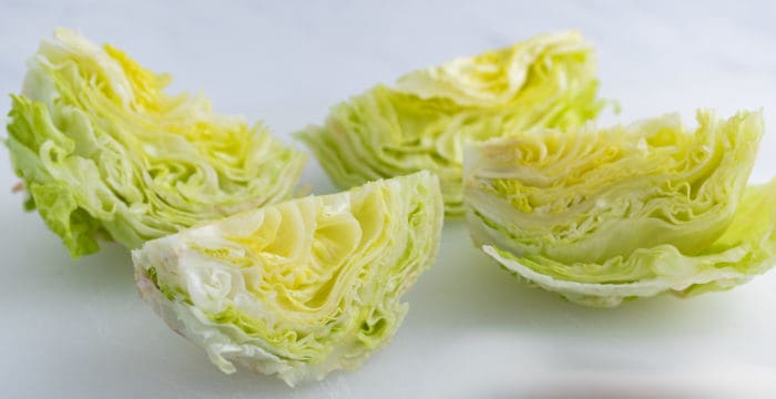 iceberg lettuce cut into four equal parts on a white cutting board