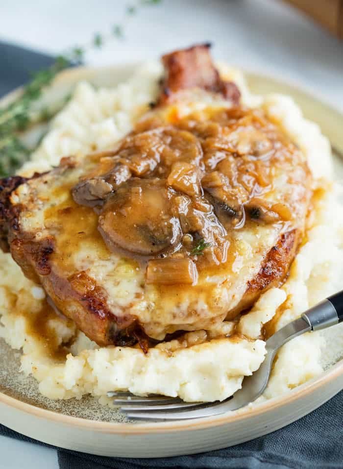 A Pork Chop on top of mashed potatoes topped with melted cheese and a french onion mushroom sauce.