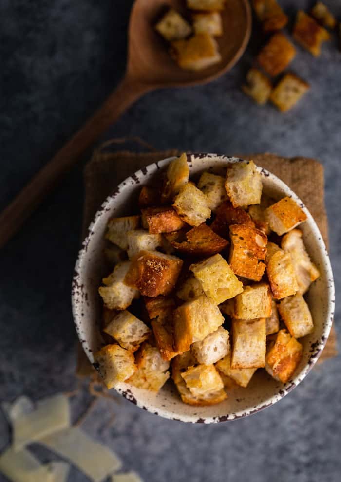 homemade croutons in a bowl on a shadowy table with a wooden spoon holding croutons on the background.