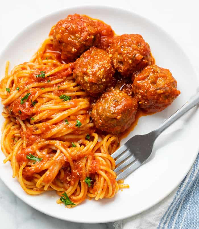 A white plate with spaghetti and slow cooker meatballs with a fork.
