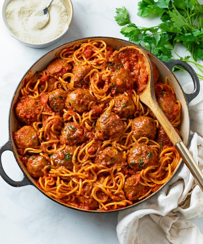 A large skillet filled with Spaghetti and Meatballs with fresh Parsley and Parmesan cheese on the side.