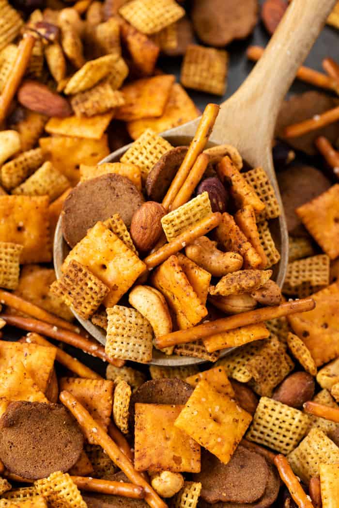 A wooden spoon scooping up Spicy Chex Mix from a baking sheet.