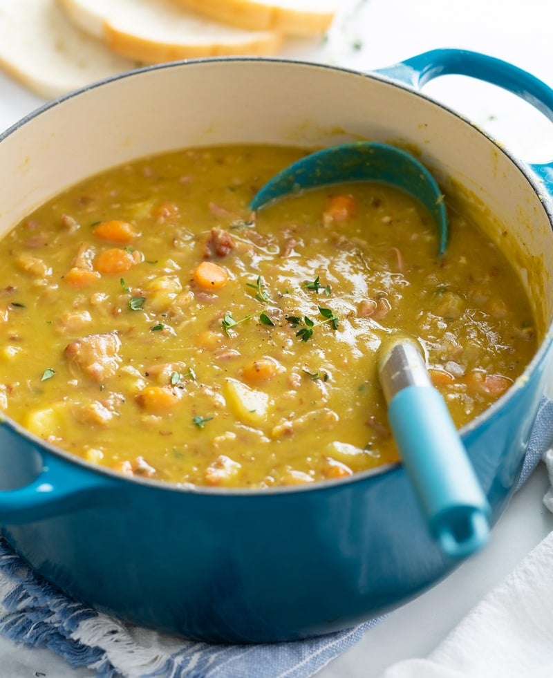 A pot of Split Pea Soup with a ladle in it and fresh thyme on top.