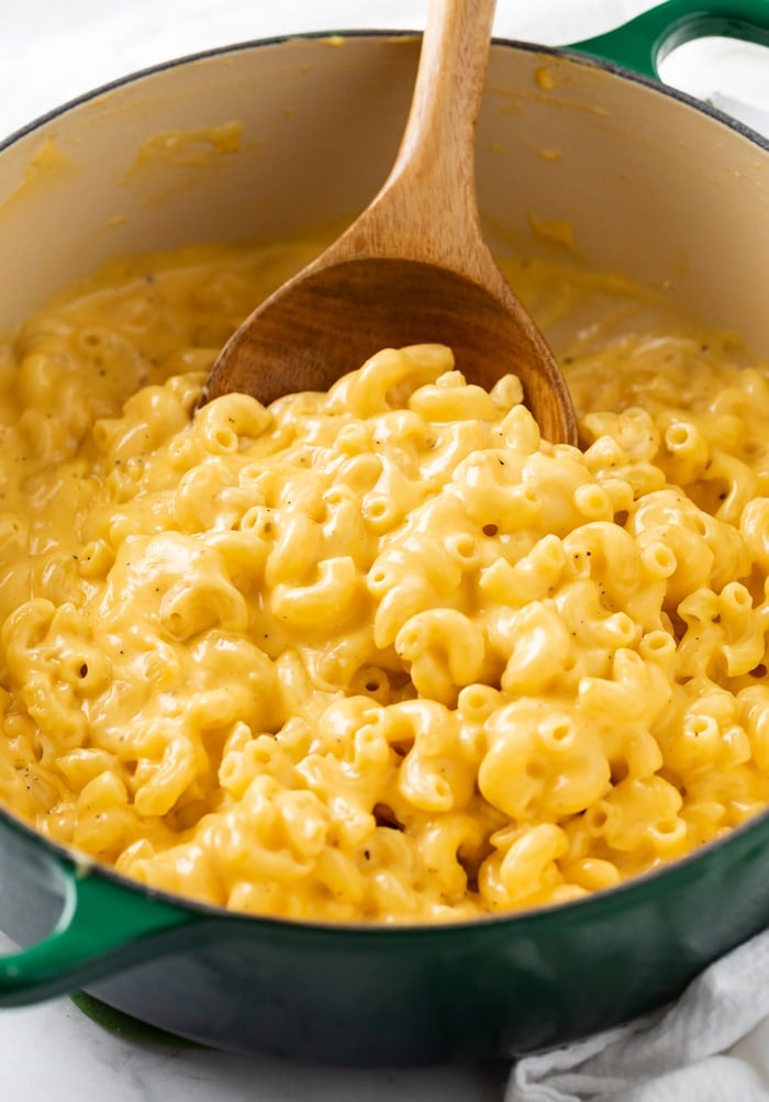 A dutch oven filled with creamy stovetop mac and cheese with a wooden spoon.
