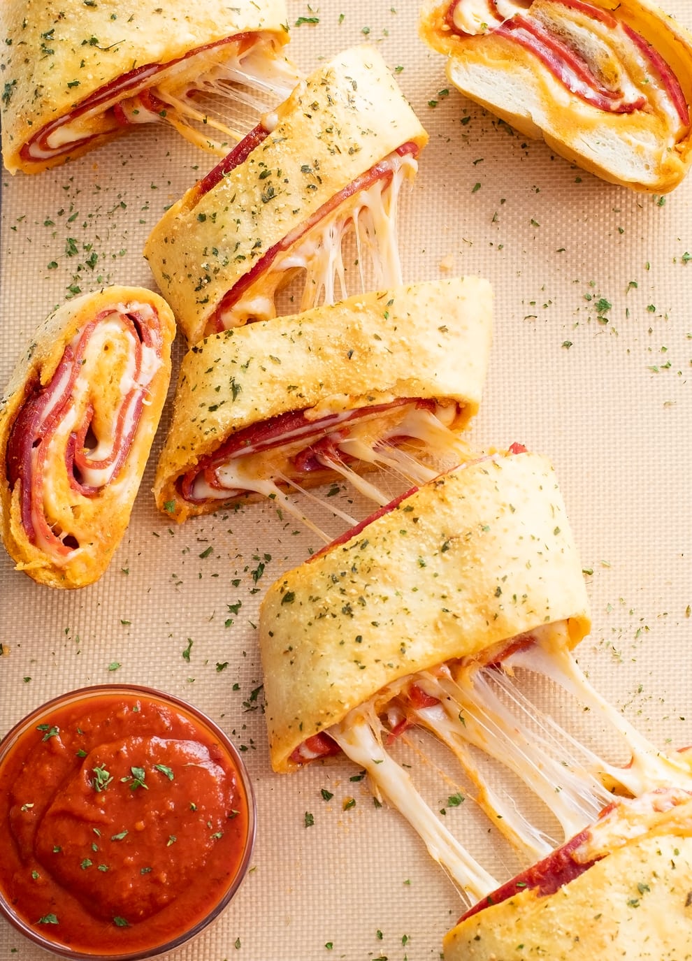 Overhead view of sliced Stromboli on a baking mat with cheese pulls and marinara sauce.