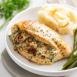 Stuffed Chicken Breast with mashed potatoes in the background and green beans on the side.