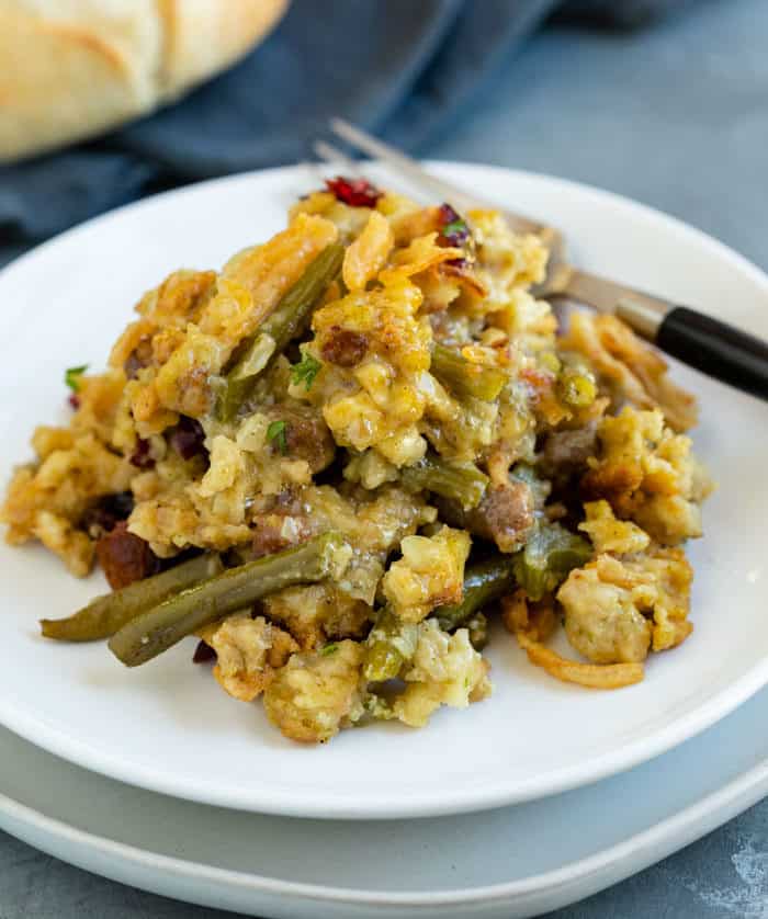 Stuffing and green bean casserole on a white plate with a fork next to it.