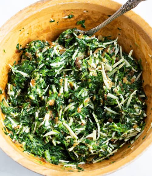 A mixing bowl of spinach pie filling ingredients mixed together.