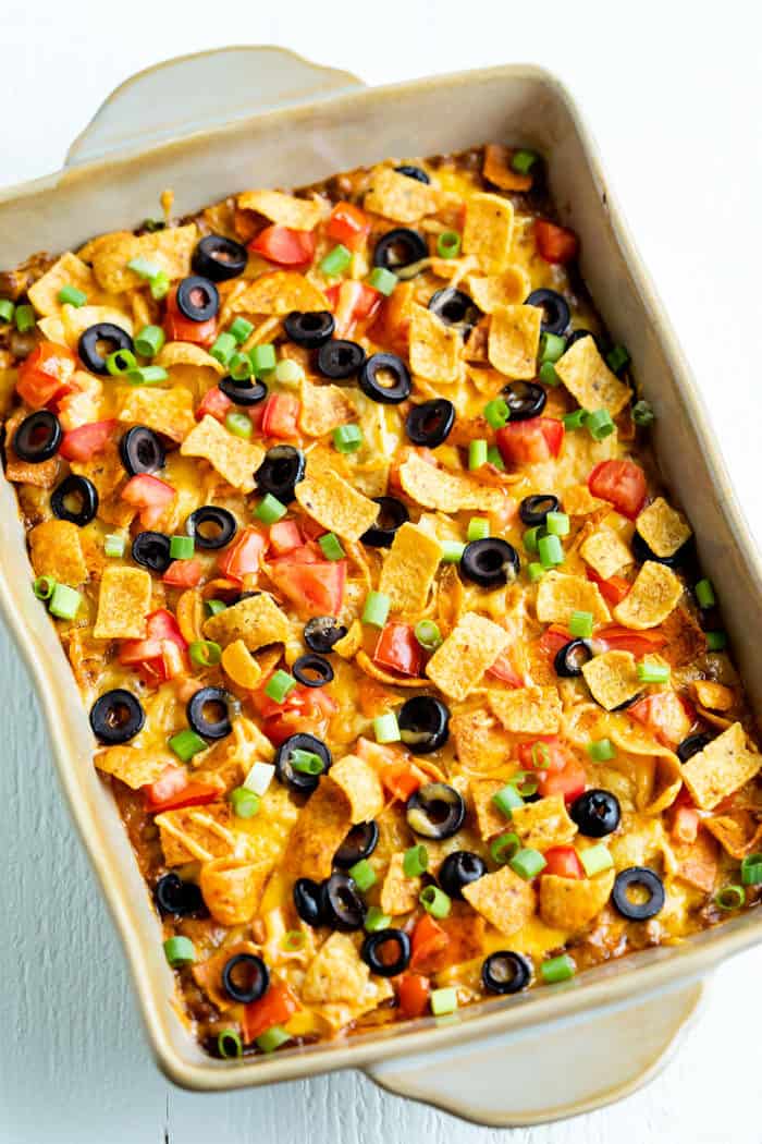 Overhead view of Taco Casserole in a casserole dish topped with fritos, tomatoes, and black olives.