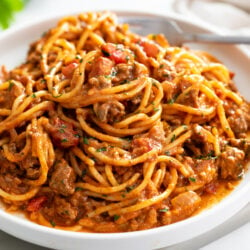 A white plate with Taco Spaghetti with taco meat and diced tomatoes.