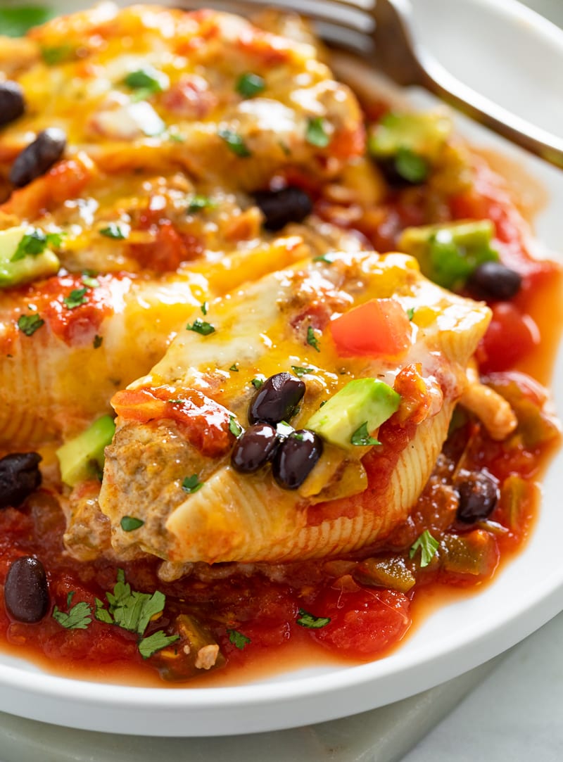 Taco Stuffed Shells on a white plate with cheese, black beans, and avocado.