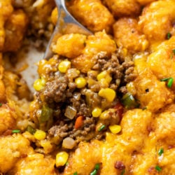 A spoon scooping up tater tot casserole with ground beef, corn, and crispy tater tots.