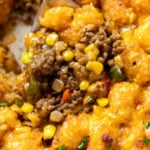 A spoon scooping up Tater Tot Casserole from a skillet with crispy tater tots and ground beef with corn.