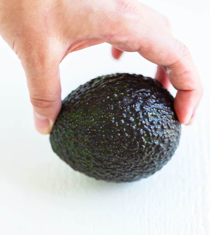 A hand holding each end of an avocado to test for ripeness.