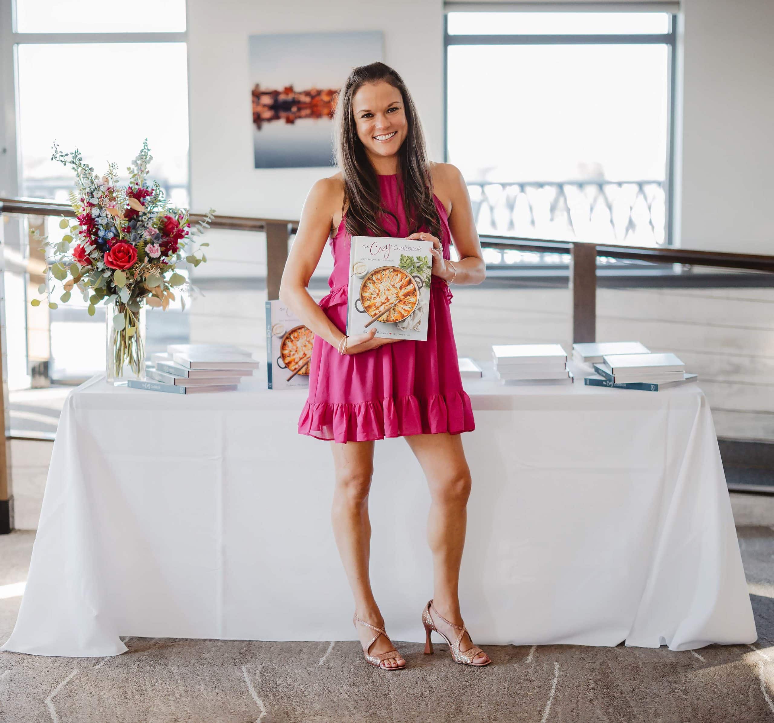Stephanie Melchione holding up The Cozy Cookbook with a table in the background.