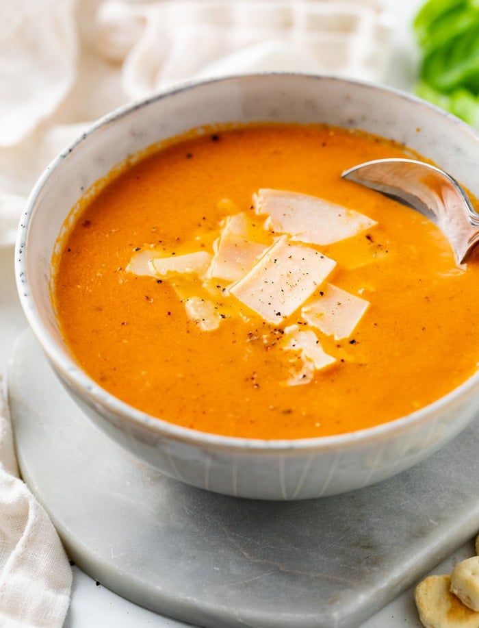 A white bowl with Tomato Soup topped with Parmesan Cheese and freshly cracked pepper.