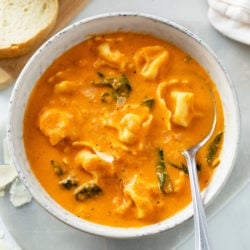 A white bowl with creamy Tomato Tortellini Soup in it with spinach.