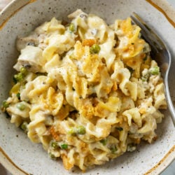 A bowl of Tuna Noodle Casserole with egg noodles in cream sauce with peas and crushed Ritz on top.