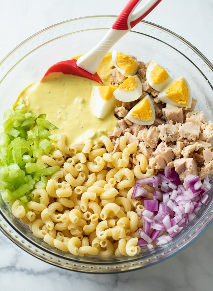 A glass bowl with ingredients for making Tuna Pasta Salad before being stirred.