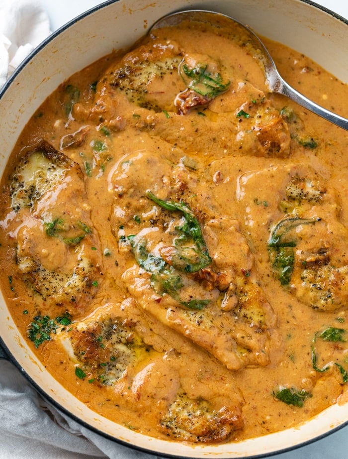A pot of Tuscan Chicken in a creamy tomato sauce with spinach.