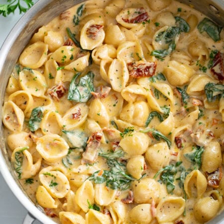 A skillet filled with creamy Tuscan Mac and Cheese with spinach and sundried tomatoes.