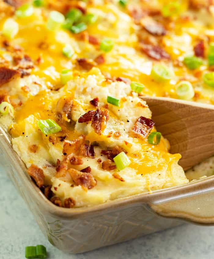 A close up image of a wooden spoon filled twice baked potato casserole in a casserole dish. 