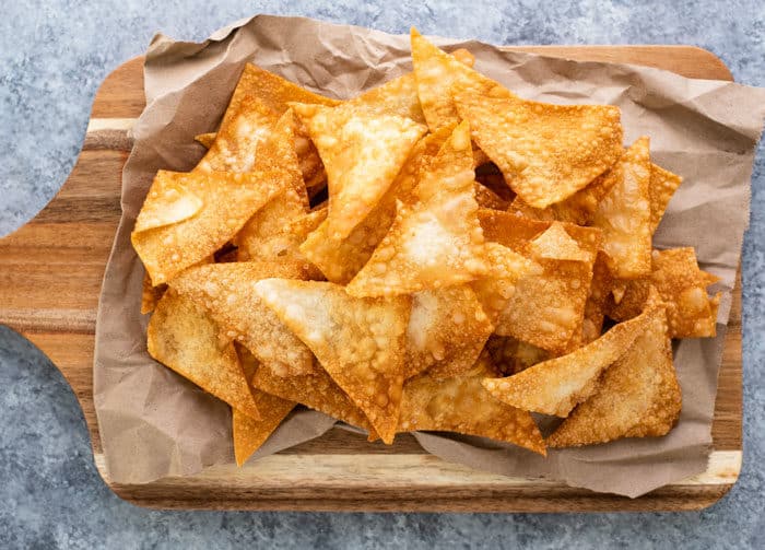Golden fried wonton chips on a wooden cutting board after being fried. 