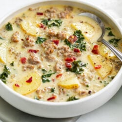 A white bowl of Zuppa Toscana Soup with bacon on top.